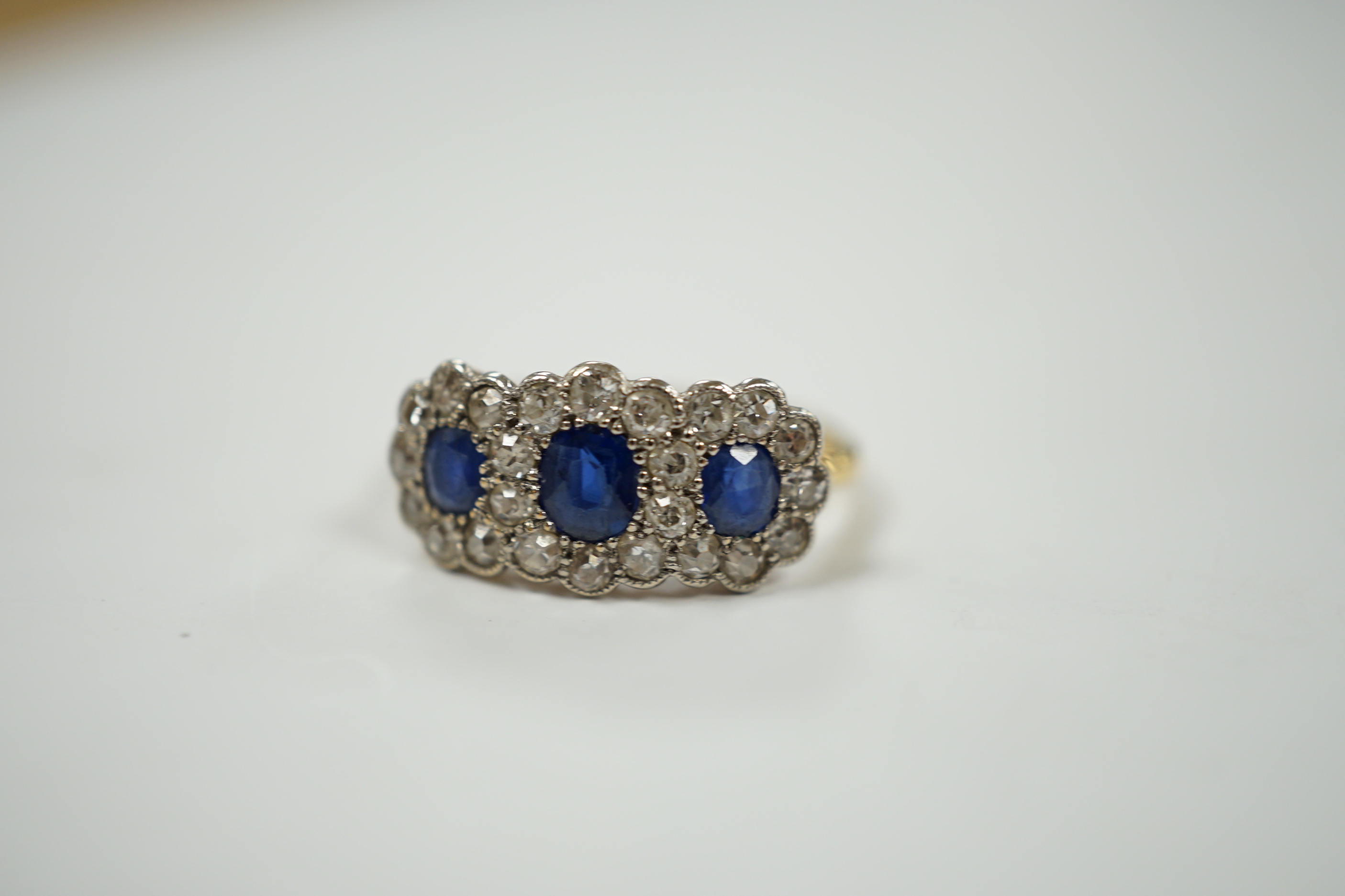 A yellow metal and millegrain set sapphire and diamond triple cluster ring, size K/L, gross weight 2.5 grams.